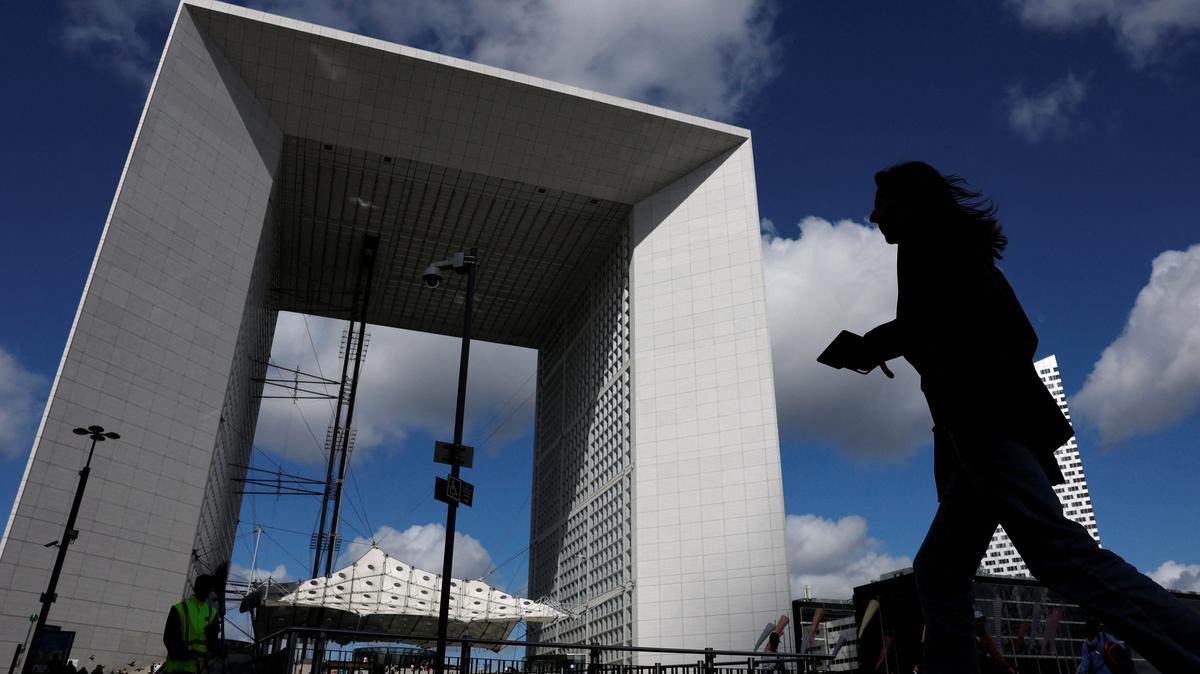 A woman, holding her mobile phone, walks past the Grande Arche at the financial and business district of La Defense in Puteaux near Paris, france, September 12, 2025. REUTERS/Stephanie Lecocq