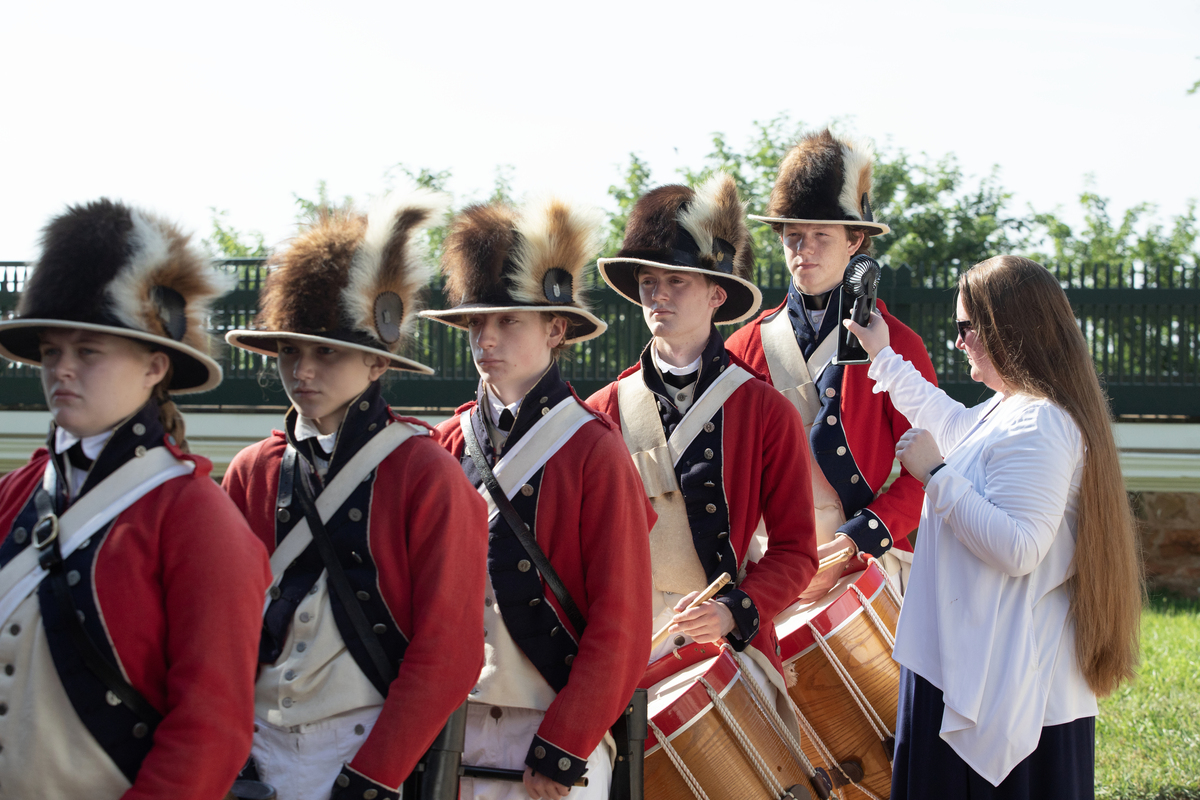 The Lewis and Clark Fife and Drum Corps is cooled down with the help of a small fan held by Director Janelle Stone-Heffner, right, during a naturalization ceremony at Monticello in Charlottesville, Va., July 4. 2026. America celebrates the 250th anniversary of its independence today, with people from one end of the country to the other marking the milestone with fireworks, parades and concerts. (Kirsten Luce/The New York Times)