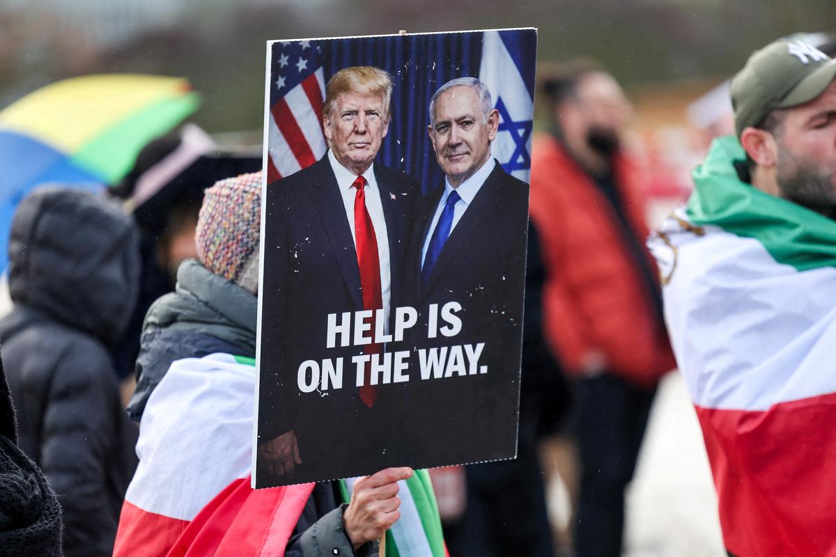 FILE PHOTO: A person holds a placard with a picture of U.S. President Donald Trump alongside Israeli Prime Minister Benjamin Netanyahu, as protesters gather near the United Nations office, on the day of the second round of nuclear talks between U.S. and Iran, in Geneva, Switzerland, February 17, 2026. REUTERS/Pierre Albouy/File Photo