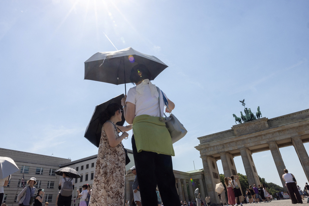 People shield themselves from the sun with umbrellas as they stand in front of the Brandenburg Gate during the ongoing heatwave in Berlin, Germany, June 27, 2026. REUTERS/Axel Schmidt