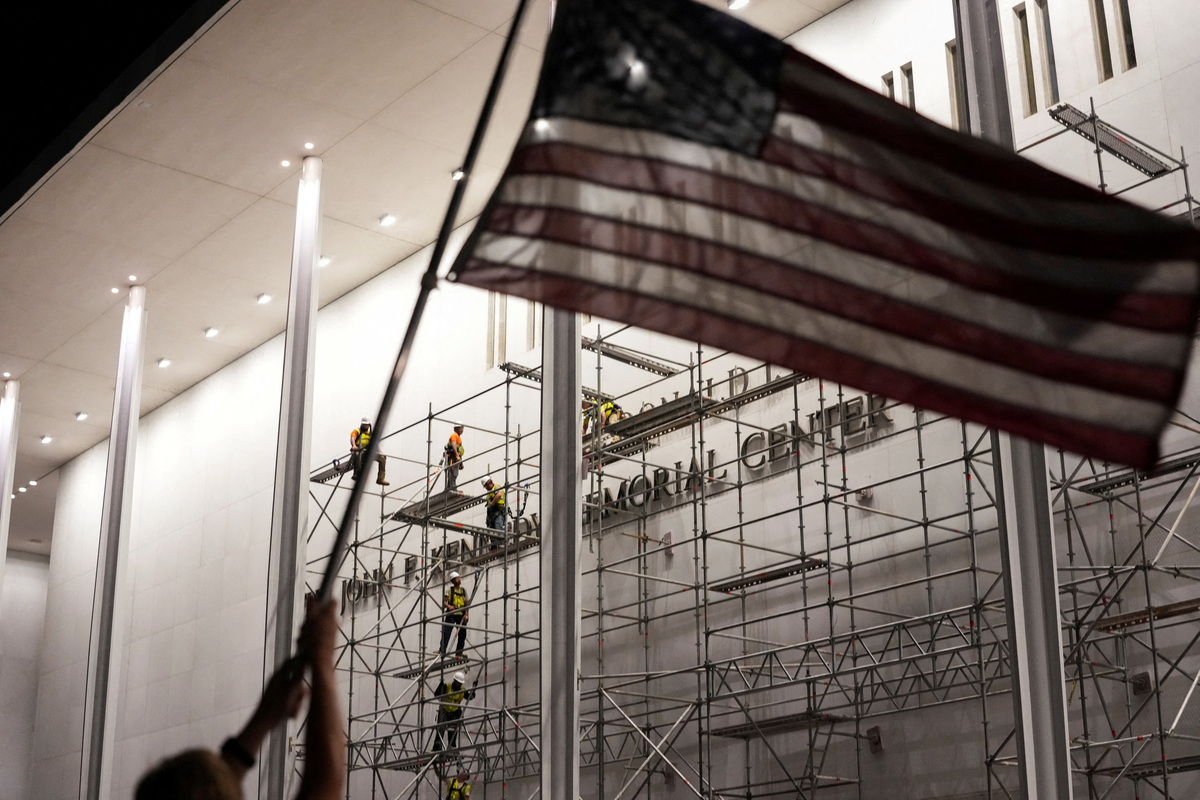 A person holds up a U.S. national flag as workers prepare scaffolding ahead of removing the lettering referencing U.S. President Donald Trump from the facade of the John F. Kennedy Center for the Performing Arts, after a federal judge ordered that President Trump's name be removed from the building in Washington, D.C., U.S., June 12, 2026. REUTERS/Ken Cedeno