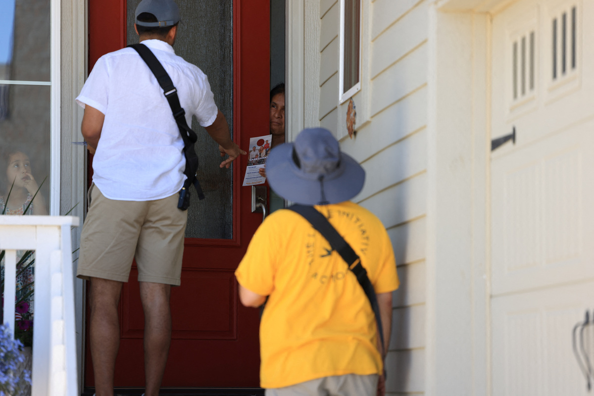 Angel Merlos of the right-leaning grassroots political organization, The LIBRE Initiative, hands a flyer to a woman while canvassing a neighborhood in Brighton, Colorado, U.S., June 11, 2026. REUTERS/Kevin Mohatt