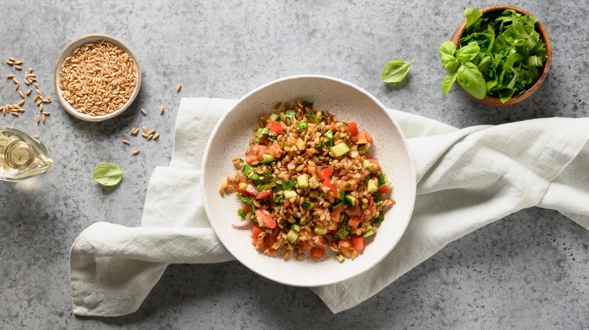 Tasty homemade salad of whole grain cereal spelt with fresh vegetables on grey table. Top view.