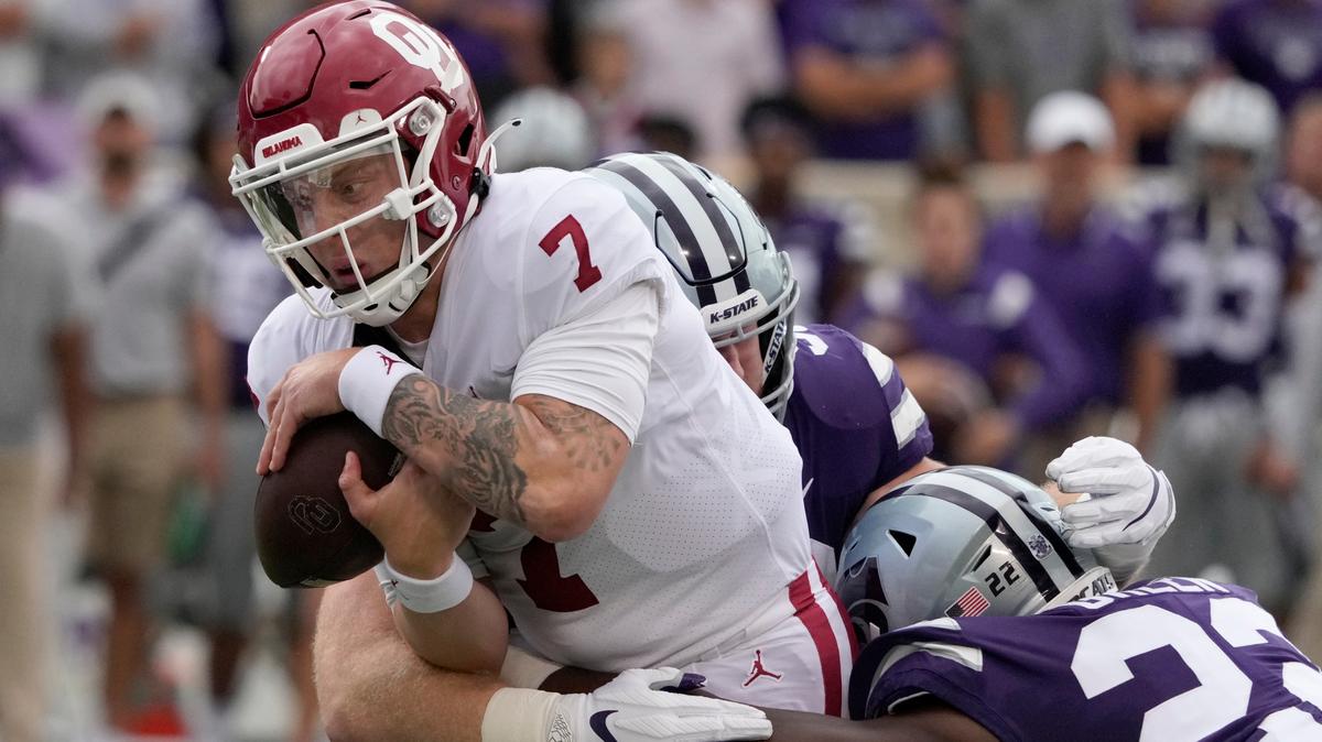 Oklahoma quarterback Spencer Rattler (7) hangs on to the ball while being tackled by Kansas State defensive back Julius Brents (23) and defensive tackle Eli Huggins (92) during the first half of an NCAA college football game in Manhattan, Kan., Saturday, Oct. 2 2021. (AP Photo/Orlin Wagner)