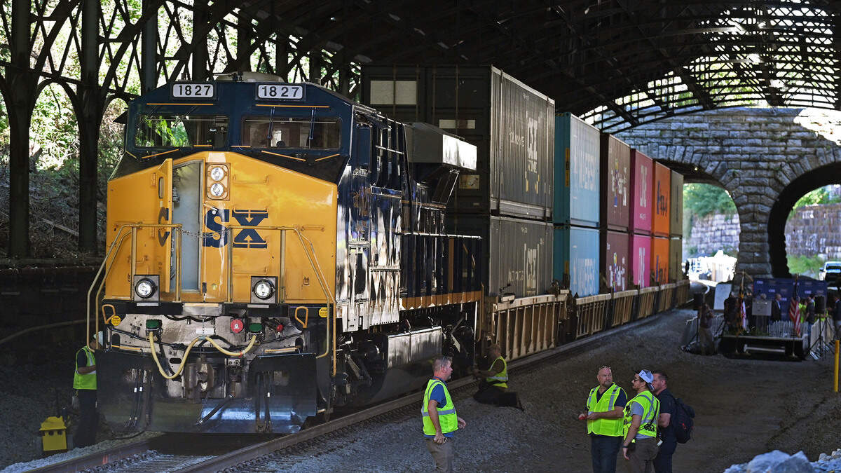 A double-stacked freight train stands as backdrop for the ceremony in September 2025 to reopen the expanded Howard Street Tunnel marking a milestone toward modernizing freight rail capacity from the Port of Baltimore throughout the East Coast.