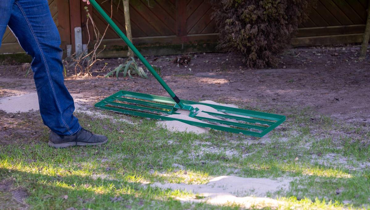  Man uses a lawn rake to put a layer of sand on the lawn. The so called topdressing levels out uneven parts and helps to ventilate the lawn. 