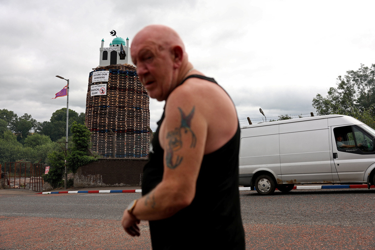 A man walks past, as an effigy of a person holding a knife in a mosque stands atop the Moygashel bonfire ahead of its lighting as part of the annual bonfire events marking the 1690 Battle of the Boyne, in Moygashel, Northern Ireland, July 9, 2026. REUTERS/Cathal McNaughton