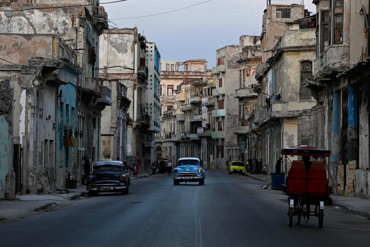 Vintage cars and a tricycle drive on a street downtown as Cuba's state-run economy has descended into a full-blown crisis after the administration of U.S. President Donald Trump hardened sanctions and cut off the Caribbean nation's oil supply, in Havana, Cuba, February 21, 2026. REUTERS/Norlys Perez