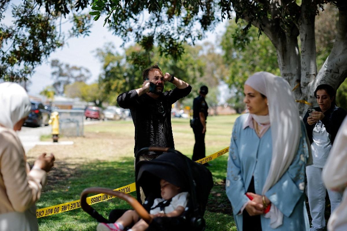Members of the Muslim community use their phones at the scene of a reported active shooter situation at the Islamic Center, with yellow tape placed behind them to cordon the area, in San Diego, California, U.S., May 18, 2026.  REUTERS/Mike Blake