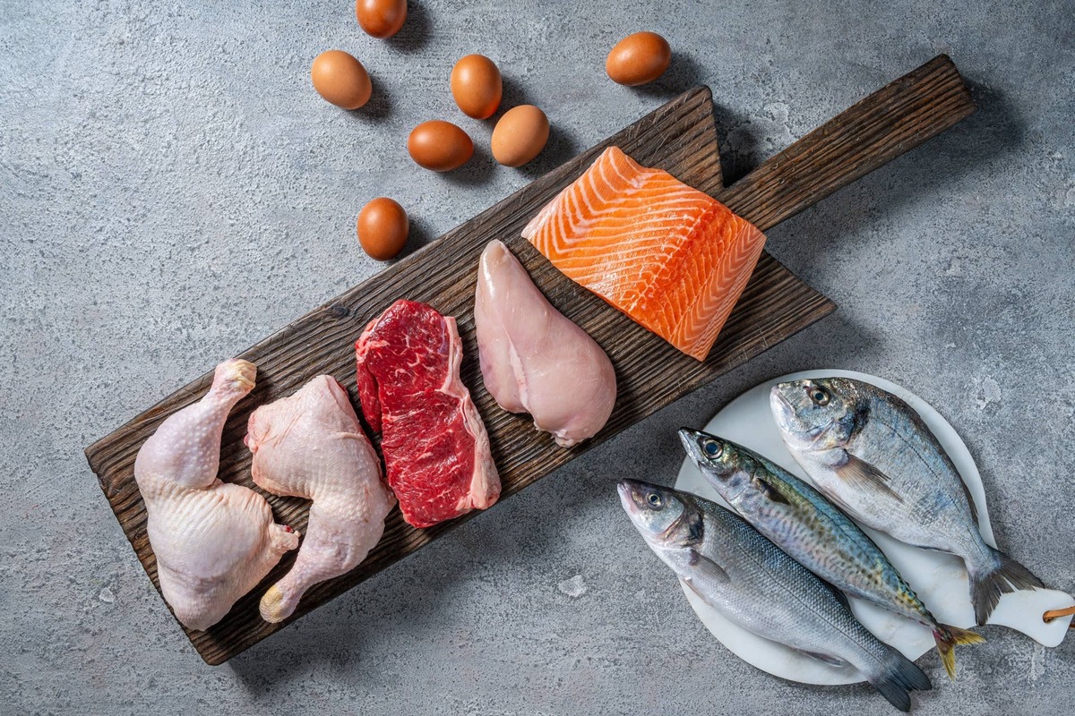  Healthy protein source food meat, eggs and fish: chicken, beaf, salmon, seabass, mackerel and sea bream on a cutting board in a gray kitchen table background.