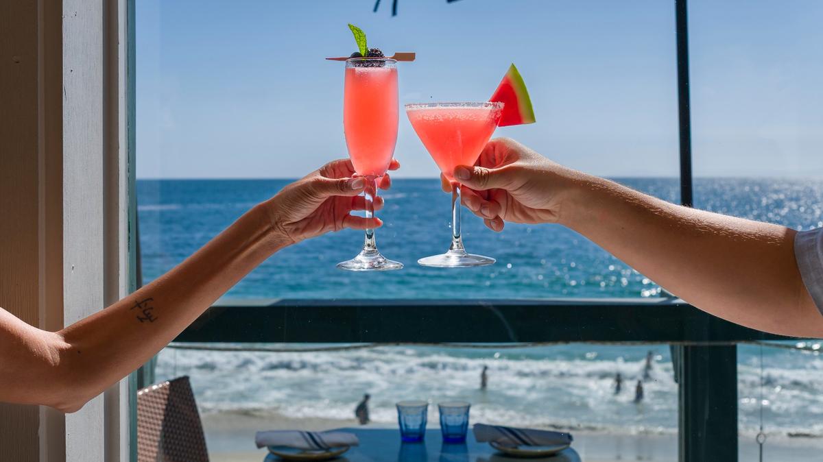 A toast with ocean views from the dining room at Driftwood Kitchen in Laguna Beach on Wednesday, May 6, 2026, with drinks, at left, Black and Blue, with blackberries, blueberries, contreau noir, and prosecco, and Nectar of the Seven Seas, with Meili vodka created by Jason Momoa, watermelon, lime juice, and salt rim. (Photo by Leonard Ortiz, Orange County Register/SCNG)