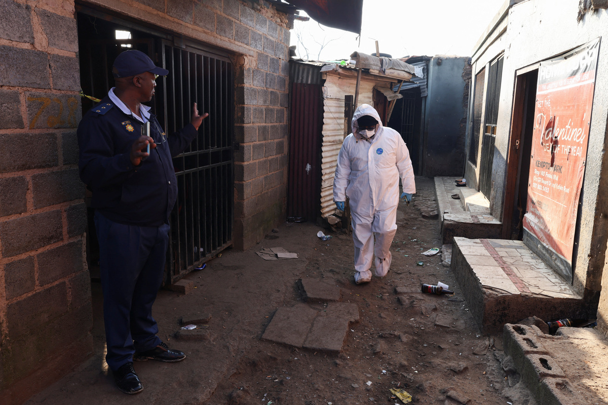 A Police oficer gestures next to a member of the forensics team after, according to the police, gunmen opened fire at an informal settlement in Cleveland, Johannesburg, South Africa,  June 10, 2026. REUTERS/Siphiwe Sibeko