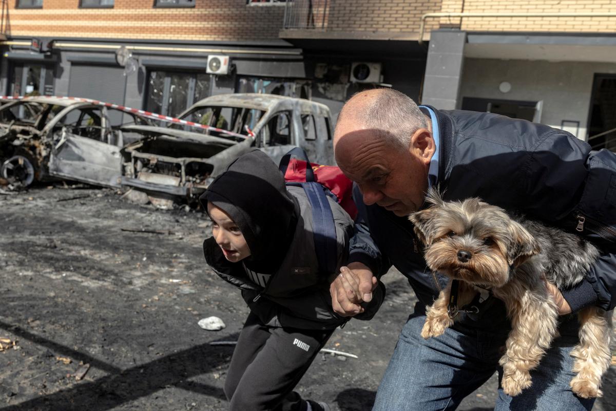 Residents carry a dog as they run from an apartment building to avoid falling glass shards after it was damaged during a night of Russian missile and drone strikes, amid Russia's attack on Ukraine, in Shchaslyve, outside Kyiv, Kyiv region, Ukraine May 14, 2026. REUTERS/Thomas Peter