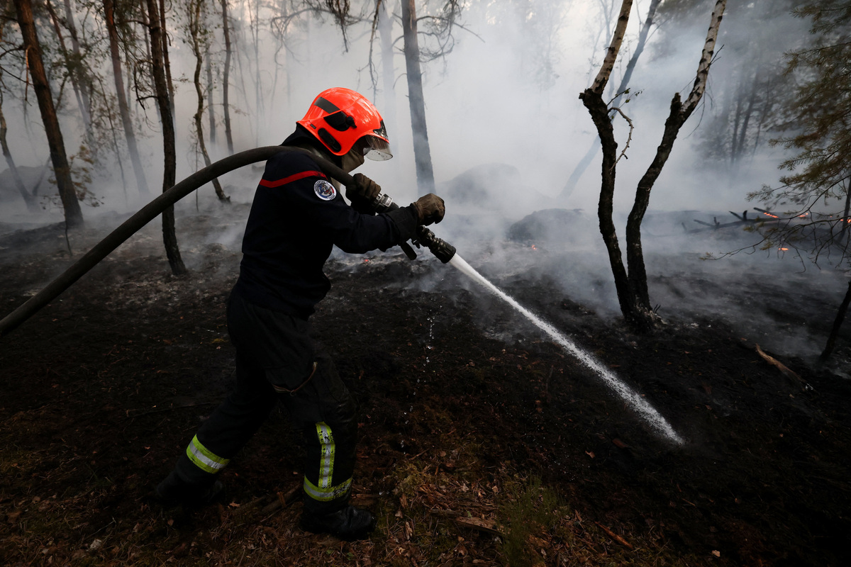 A firefighter sprays water to extinguish flames in the Fontainebleau forest during a wildfire, in Noisy-sur-Ecole, near Paris, during a heatwave affecting large parts of France, July 13, 2026. REUTERS/Stephane Mahe