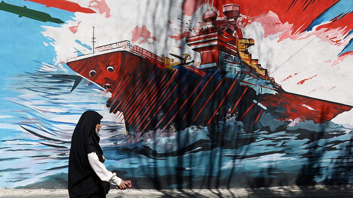 A woman walks next to a mural of a battleship on a street in Tehran, Iran, on Monday. President Donald Trump on Tuesday threatened to resume strikes on Iran in the coming days as part of the push for a deal to end the war, after he said he had just called off a U.S. attack.