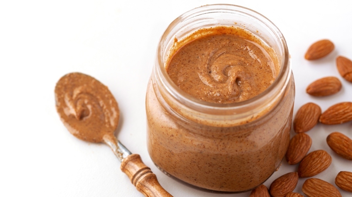 Organic almond butter with raw almonds in a glass jar on a white background with copy space