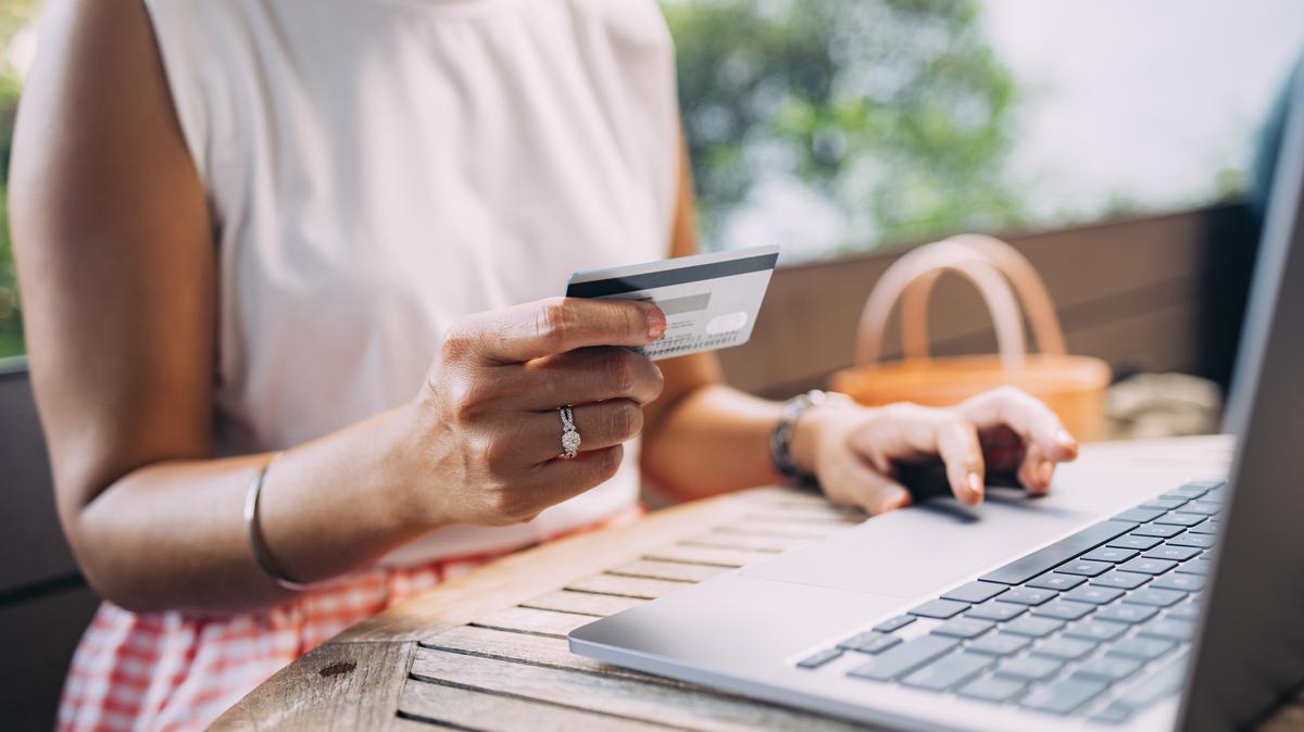An anonymous Asian female holding her credit card while paying something online on her computer.