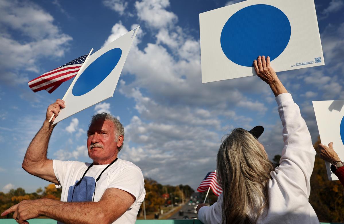  Demonstrators wave “Blue Dot” signs from a pedestrian bridge over rush hour traffic on October 24, 2024, in Omaha, Nebraska. 