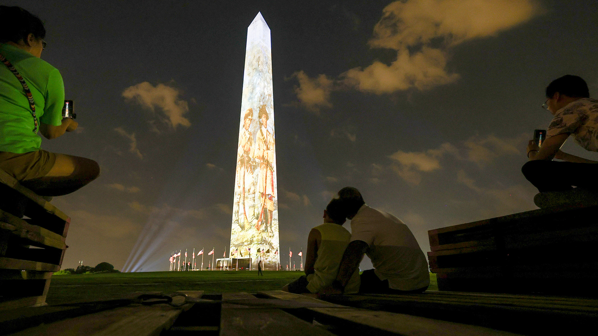People gather to watch a light show projected onto the Washington Monument on July 1, 2026, in Washington, D.C. The monument will be lit up for 18 minutes every night until July 5th in celebration of America's 250th. (Finn Gomez/Getty Images/TNS)