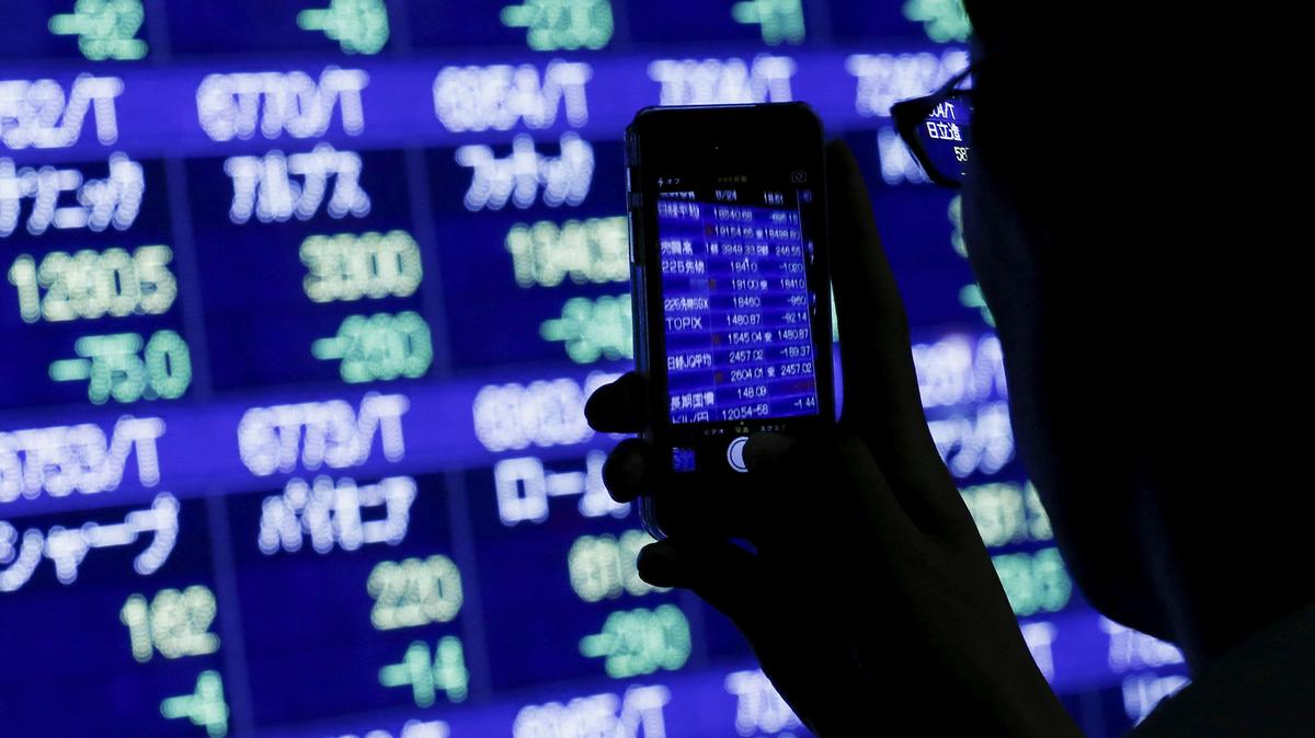 FILE PHOTO: A man uses his phone to take pictures of market indices at a stock quotation board outside a brokerage in Tokyo, August 24, 2015.  REUTERS/Thomas Peter/File Photo
