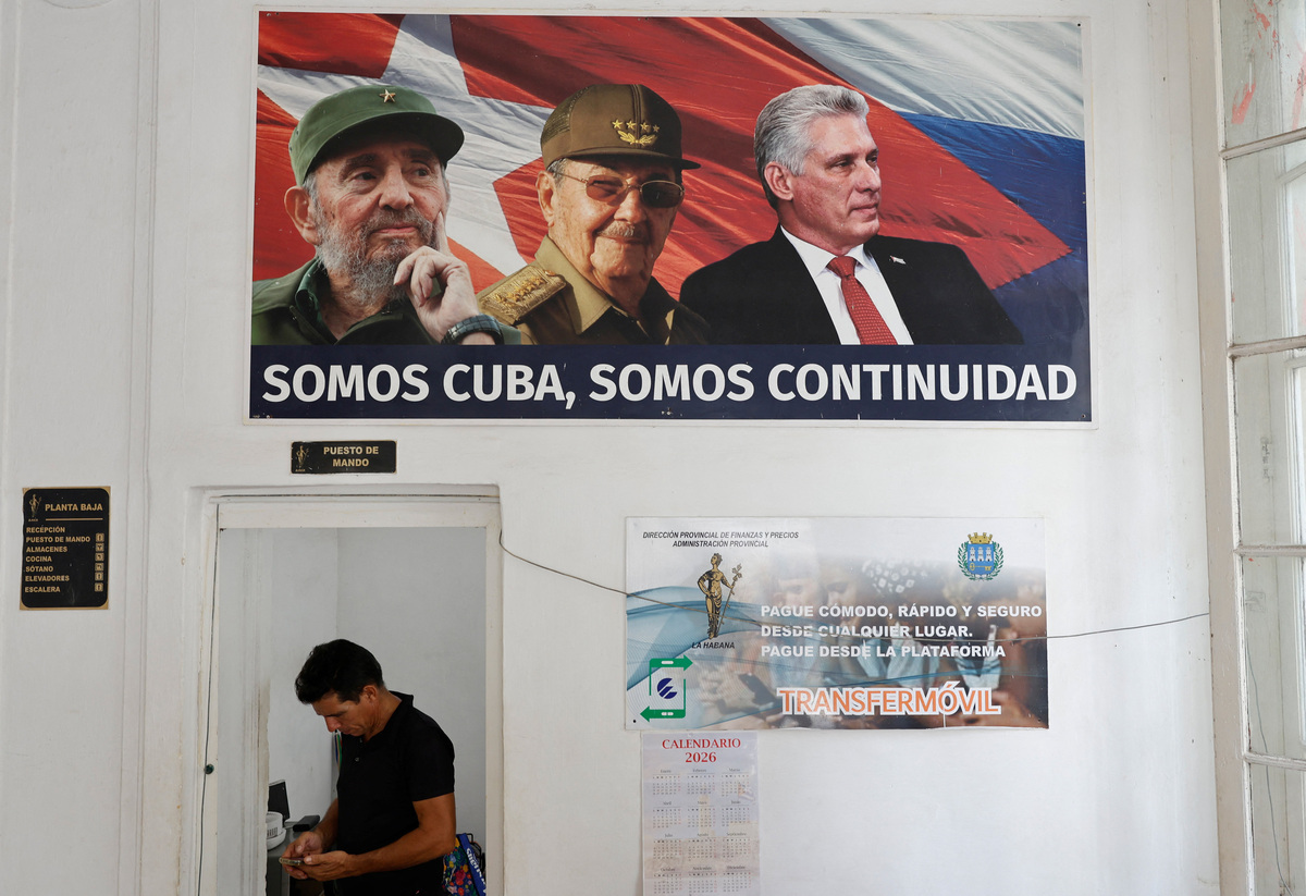 A man checks his phone at an office of the Ministry of Finance and Prices underneath a framed poster of Cuba's late President Fidel Castro, his brother, former President Raul Castro and President Miguel Diaz-Canel as the country marks Raul Castro's 95th birthday after U.S. authorities charged him with murder in connection with the downing of civilian airplanes in 1996 and amid sanctions and a fuel blockade by the administration of U.S. President Donald Trump, in Havana, Cuba, June 3, 2026. The writing on the poster reads “We are Cuba, we are continuity.”  REUTERS/Norlys Perez