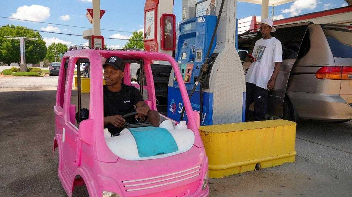 Mali Hightower, 30, poses with what he describes as a self-created gas saver, a pink Power Wheels Barbie Dream Camper, at a gas station in Ellenwood, Georgia, on Monday. The soaring cost of gasoline is reshaping everyday decisions and inspiring creative workarounds in households across the country.