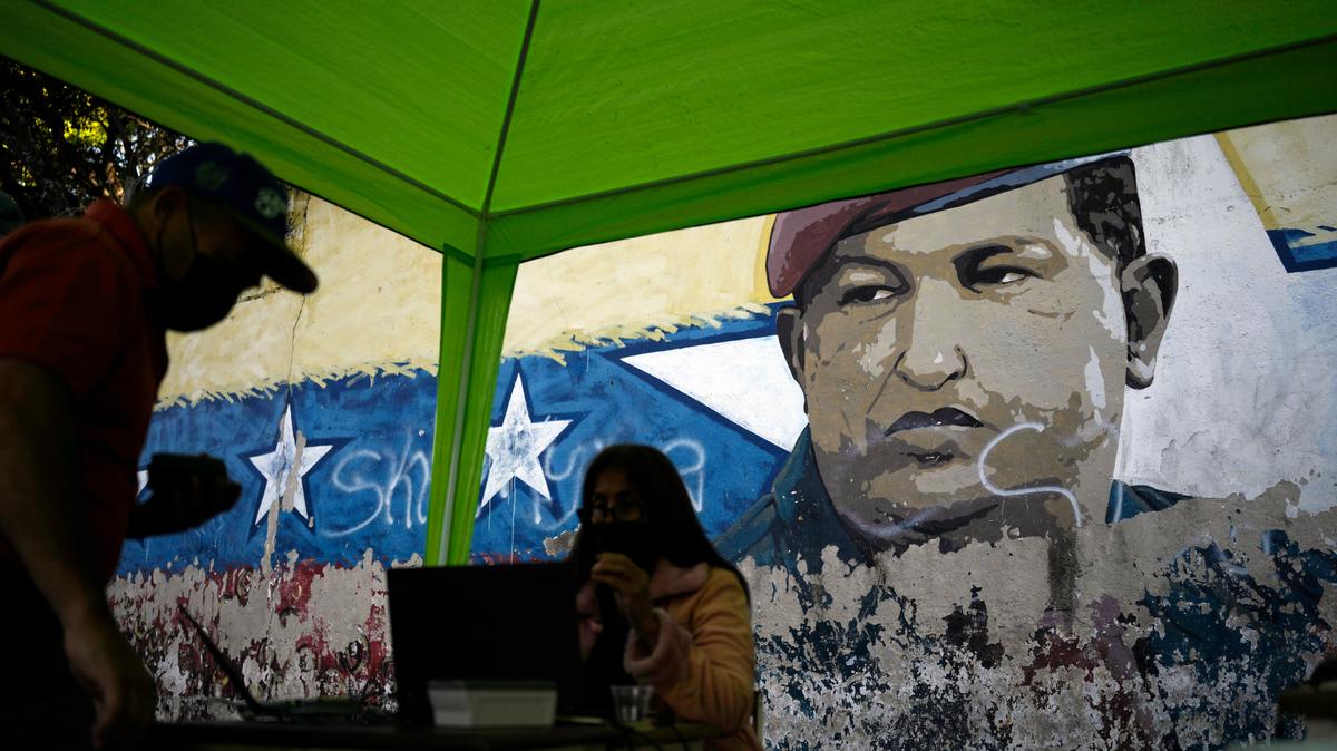 Un mural del difunto presidente Hugo Chávez decora una pared de la calle donde se instaló una mesa por parte del Consejo Nacional Electoral (CNE) para que las personas pueden firmar una petición a favor de la realización de un referéndum revocatorio de mandato del presidente Nicolás Maduro, en Caracas, Venezuela, el miércoles 26 de enero de 2022. (Foto AP/Matías Delacroix)