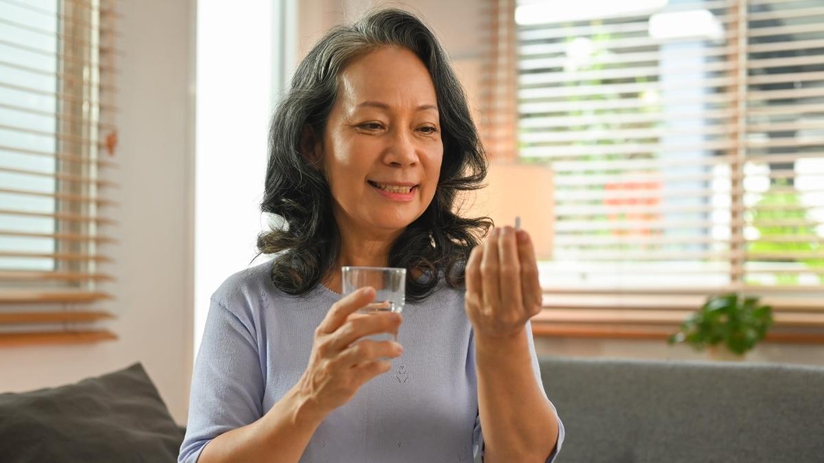 Healthy happy mature woman holding pill and glass of water. Pharmaceutical healthcare treatment concept.