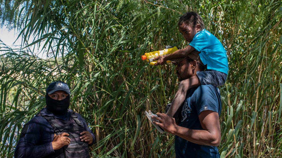 Un inmigrante haitiano, cargando a su hijo, habla con un agente policial mexicano que bloquea el paso al Río Grande, de manera que los inmigrantes no puedan cruzar la frontera con Estados Unidos, el jueves 23 de septiembre de 2021, en Ciudad Acuña, México. (AP foto/Félix Marquez)