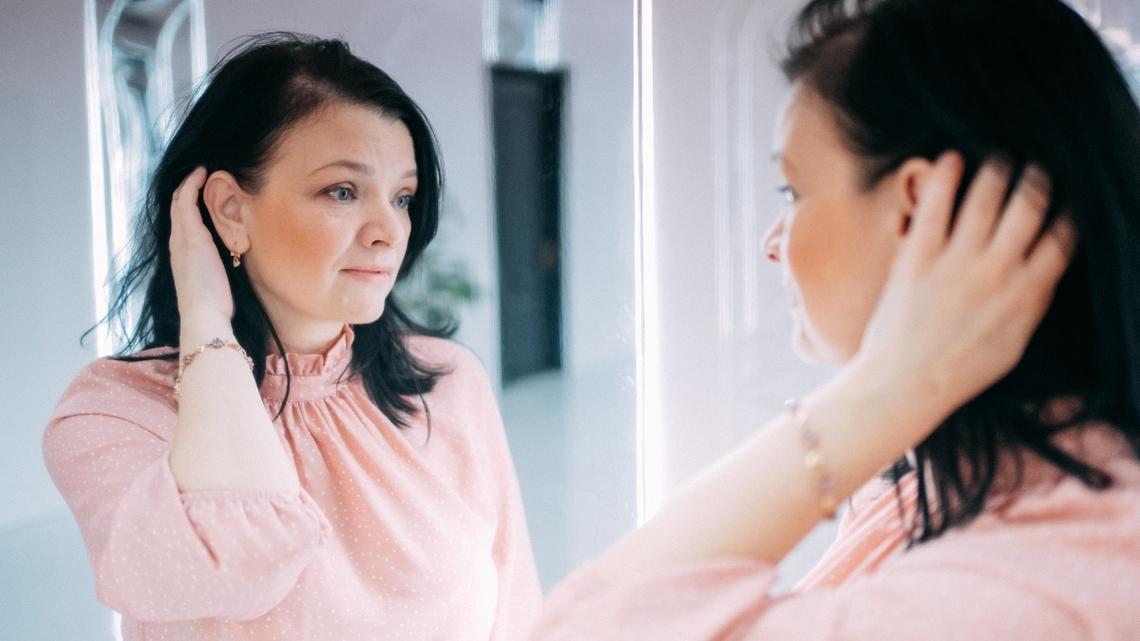 Woman looking at herself in a mirror, touching her dark hair thoughtfully