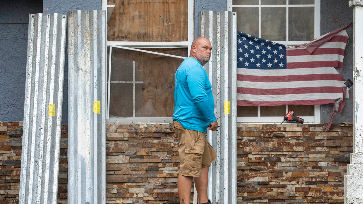 Brian Boots puts up shutters to cover damaged windows after a tornado Hurricane Milton damaged a friend's house. Boots and others pitched in to clean up the damage on October 10, 2024 in The Acreage, Florida.