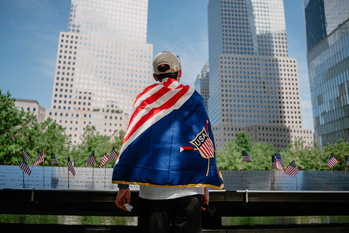 A man wearing an American flag draped over his shoulders pauses at the National September 11 Memorial in New York, July 4, 2026. America celebrates the 250th anniversary of its independence today, with people from one end of the country to the other marking the milestone with fireworks, parades and concerts. (Lucia Vazquez/The New York Times)