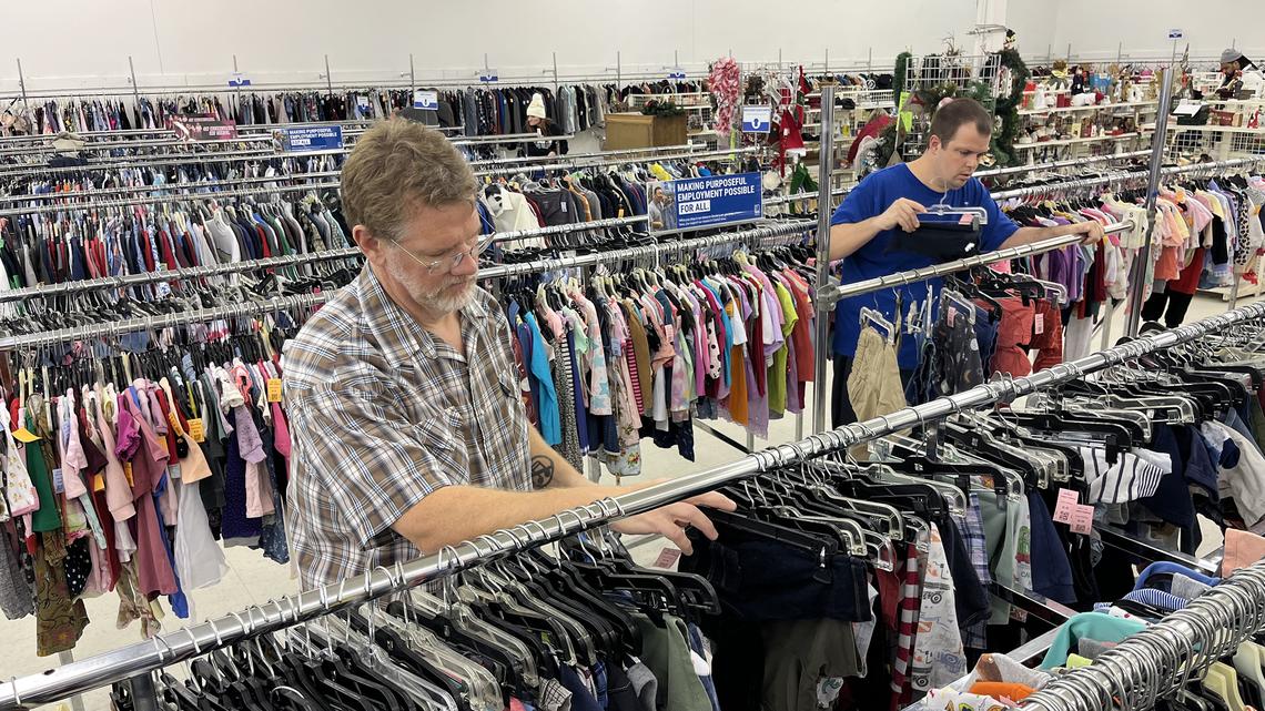 Medicaid participant Sam Walker (right) sorts clothing at a Goodwill store in Ottumwa, Iowa, with Andy Koettel, a caregiver paid through a Medicaid waiver program that helps people with disabilities. The assistance of such workers helps people like Walker live in their own homes and participate in their communities rather than be sent to institutions. (Tony Leys/KFF Health News/TNS)