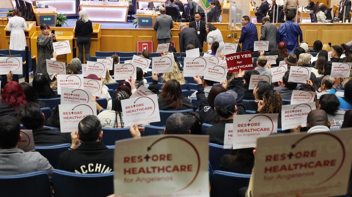 LOS ANGELES, CA FEBRUARY 10, 2026 -- Members of the audience hold up signs inside the Hall of Administration meeting room, where a motion that would place a temporary ½ percent sales tax measure (set to end in 2031) on the June primary ballot to help address more than $2.4 billion in federal funding cuts to the Los Angeles County healthcare system was being discussed on Tuesday, Feb. 10, 2026. (Myung Chun / Los Angeles Times)