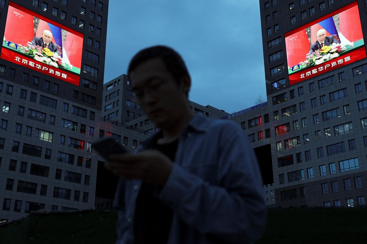 A pedestrian stands near giant screens showing news footage of Russian President Vladimir Putin at the Great Hall of the People during a state visit to China, in Beijing, China May 20, 2026. REUTERS/Florence Lo