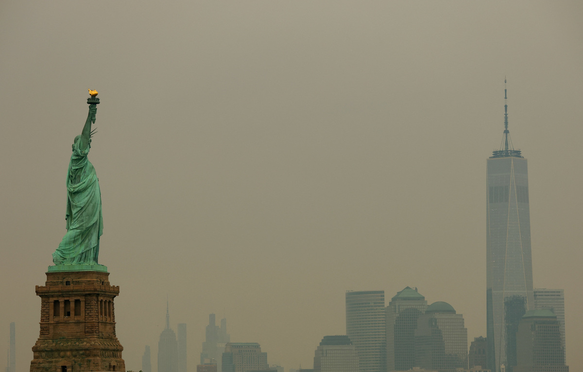 The Statue of Liberty in Jersey City, New Jersey, and the One World Trade Center tower in New York City are seen through a cover of wildfire smoke from New York Harbor, U.S., July 16, 2026. REUTERS/Mike Segar