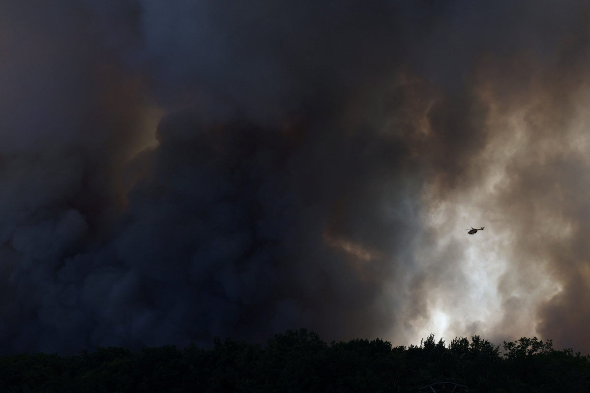 A firefighting helicopter flies through plumes of smoke above the Fontainebleau forest as a wildfire burns near Paris during a heatwave affecting large parts of France, July 13, 2026. REUTERS/Stephane Mahe