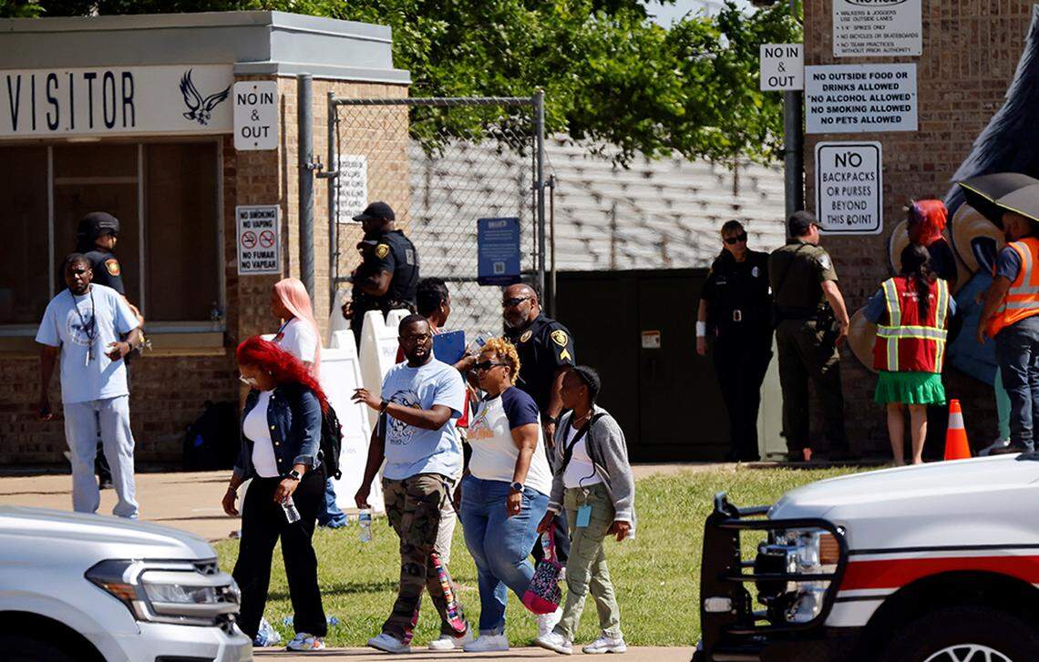 Parents of Wilmer-Hutchins High School students leave a nearby stadium in Dallas with their children following a Tuesday shooting that left at least four students injured.