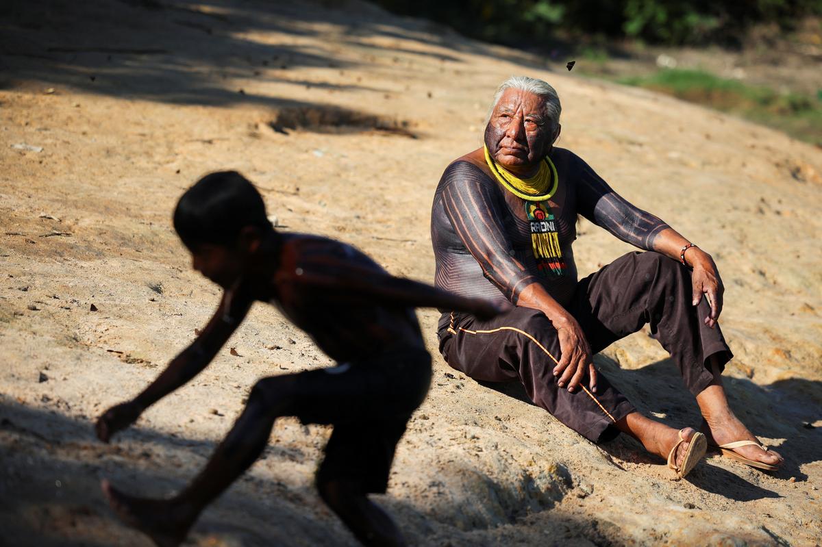 Indigenous leader Megaron Txucarramae interacts with children playing in a river while attending an interview with Reuters in the village of Pykany in the Menkragnoti Indigenous Territory of the Kayapo people, Para state, Brazil May 20, 2026. REUTERS/Adriano Machado