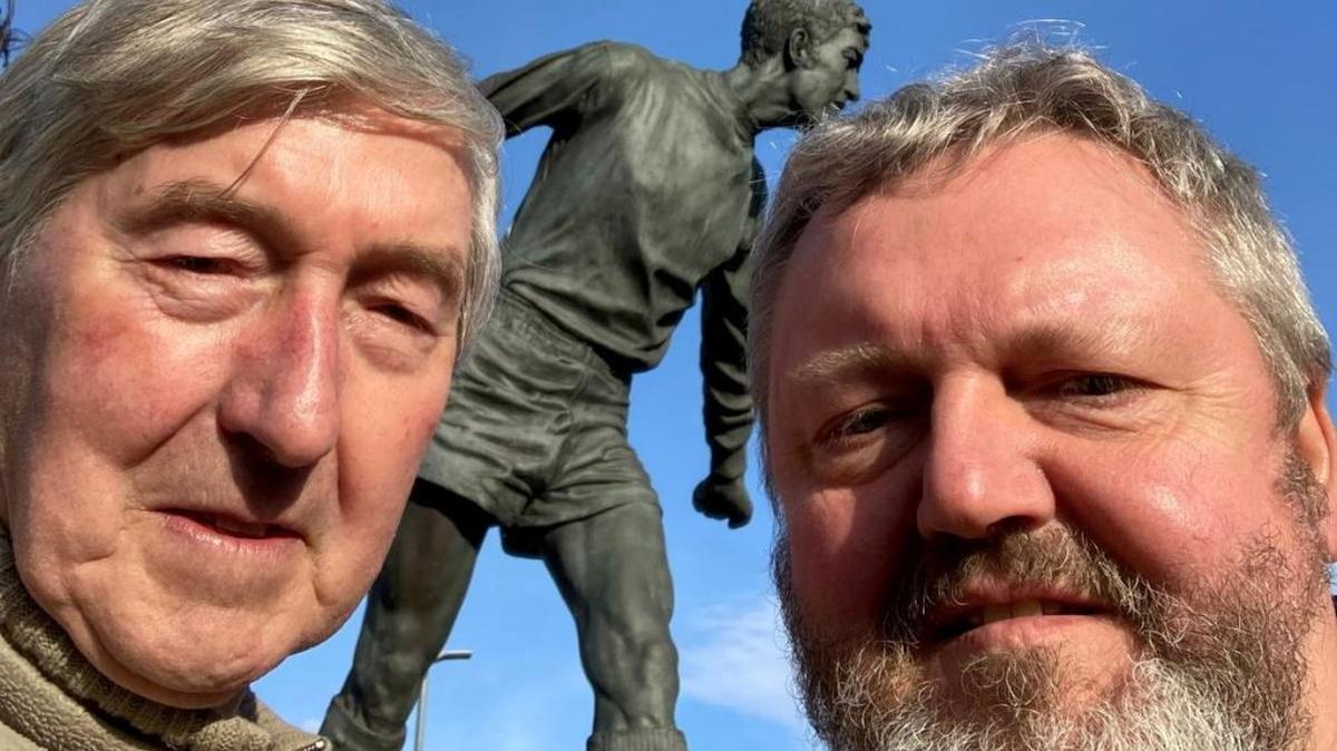 Hugh "Hughie" McIlmoyle with son Alan in front of a statue of Hugh "Hughie" McIlmoyle outside Brunton Park, the home of Carlisle United. (Alan McIlmoyle via SWNS). 
