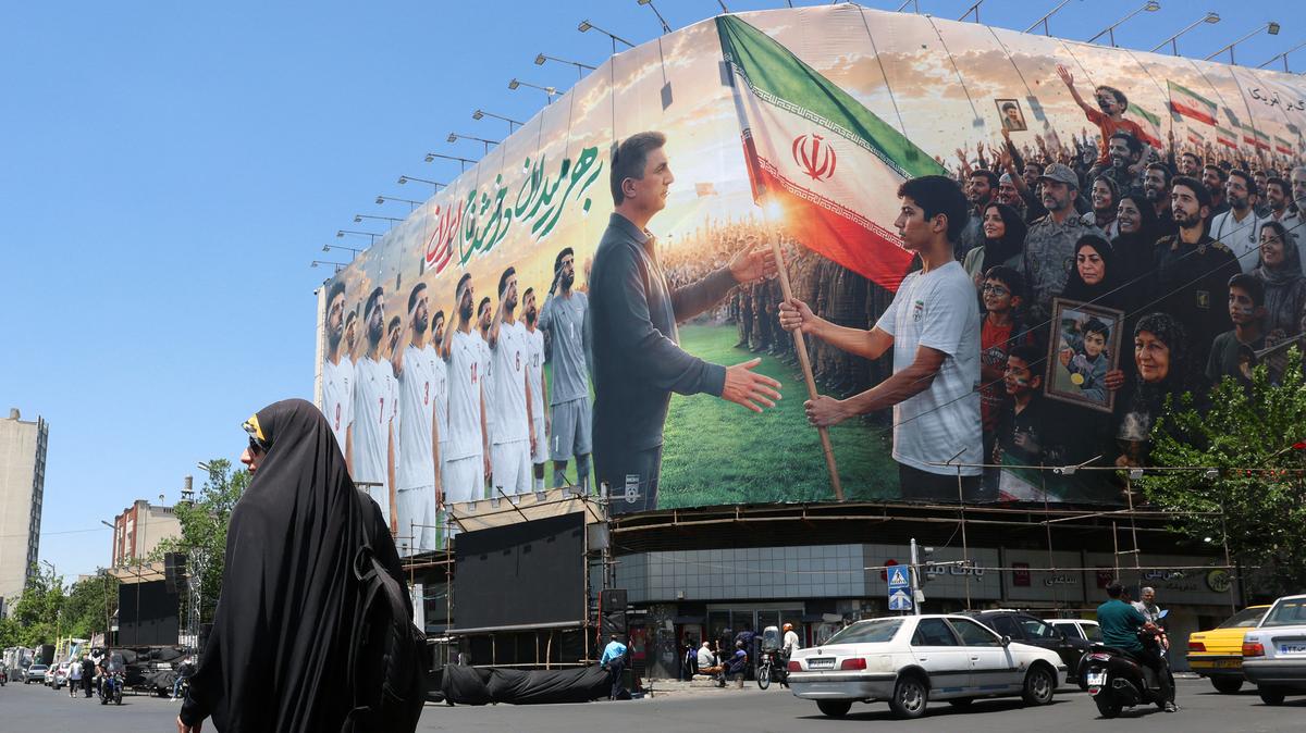 An Iranian woman walks past a huge billboard supporting Iran's national football team in the upcoming 2026 World Cup, installed on a building at Enghelab Square in Tehran on May 18, 2026. Iran has maintained its intention to participate in the tournament despite months of hostilities with the U.S. and Israel, which launched military attacks on the Middle Eastern nation in February.