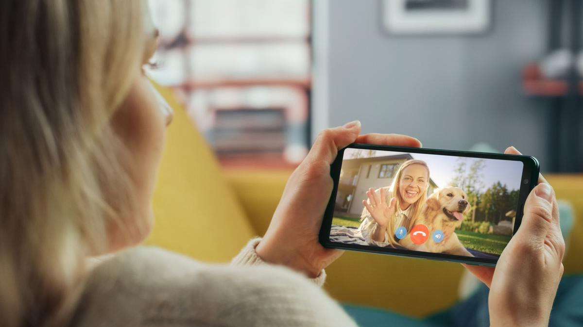 A stock image of a woman holding her phone and video calling with another person and dog. 