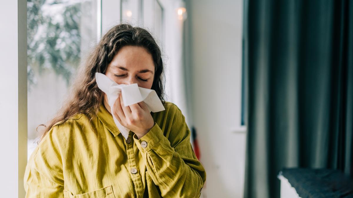 Sick woman blowing her nose with tissue paper at home, suffering from allergy or flu