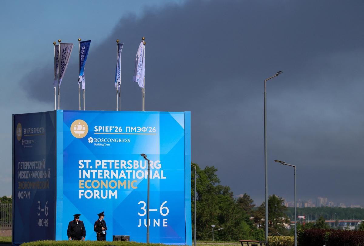 Police officers stand in front of a banner and flags with the logo of the St. Petersburg International Economic Forum (SPIEF) as heavy smoke billows in the background after drones hit infrastructure, according to the governor Alexander Beglov, in St Petersburg, Russia June 3, 2026. REUTERS/Stringer