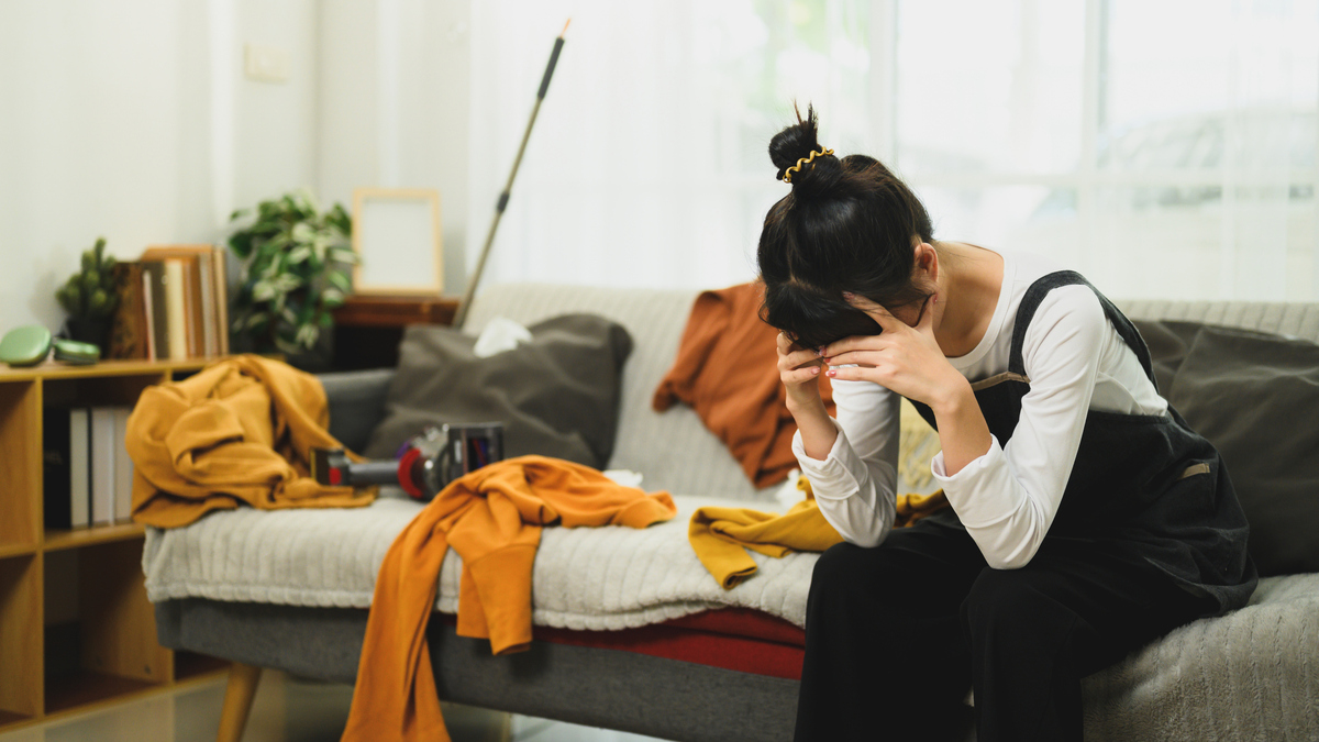 A stock image of an exhausted woman taking a break during house cleaning in messy living room.
