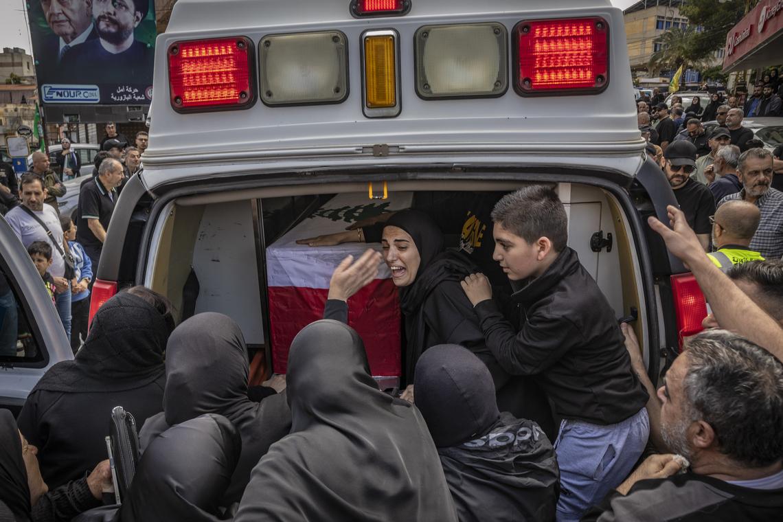 Family members grieve over a loved-one's coffin draped in the Lebanese flag as a convoy of ambulances arrive in the southern Lebanese village of Bazourieh for a mass funeral, on Monday, April 20, 2026. Families gathered for the funeral of nine people -- both Hezbollah fighters and civilians -- who were killed in recent weeks (David Guttenfelder/The New York Times)