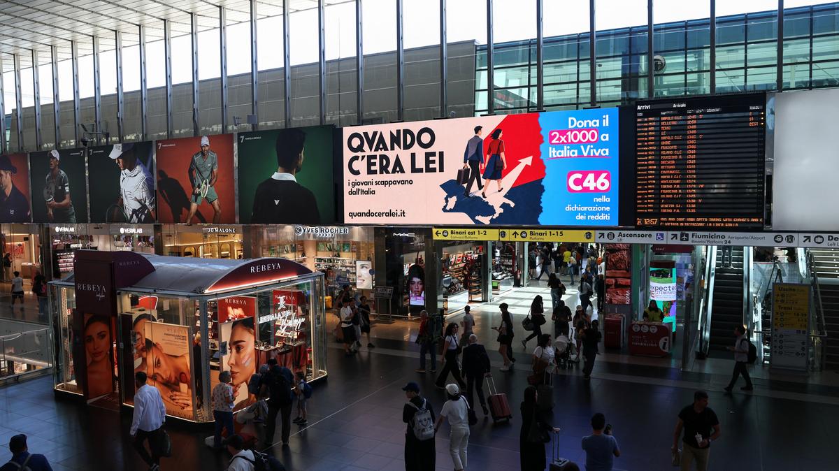 People walk past an advertisement, commissioned by Italia Viva at Roma Termini railway station, referring to Italian Prime Minister Giorgia Meloni, reading in English, "When she was around, young people were leaving Italy" and featuring imagery and typography reminiscent of Italian fascist-era propaganda from the 1930s, in Rome, Italy, May 22, 2026. REUTERS/Yara Nardi