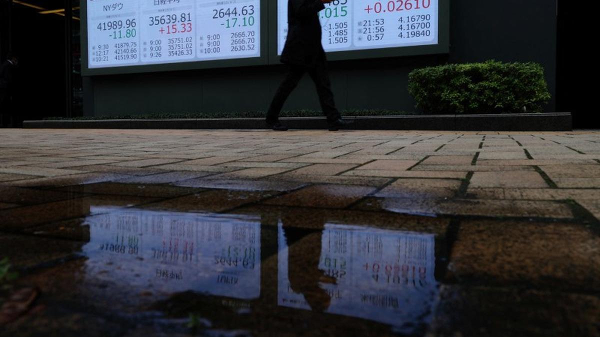 A man walks past a stock quotation board showing the Dow Jones Industrial Average, Nikkei share average, Topix average, Japan and U.S 10-year government bond yield outside a brokerage in Tokyo, Japan April 2, 2025. REUTERS/Kim Kyung-Hoon