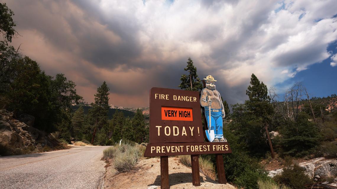 A sign with Smokey the Bear warns of a very high fire danger for the day as smoke rises from the Trout Fire burning in the Domeland Wilderness of Sequoia National Forest, near Inyokern, California on July 19, 2024. (David Swanson/AFP via Getty Images/TNS)