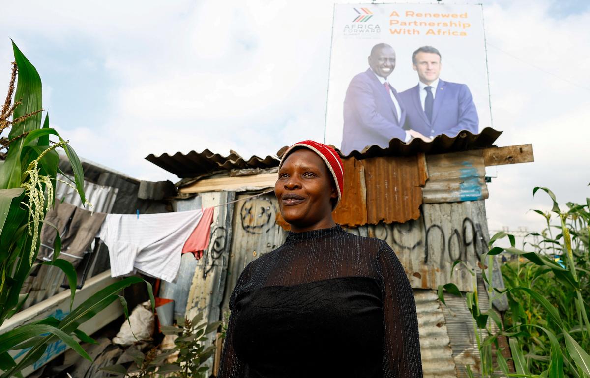 Mary Wangui Kabuki, 35, stands next to her tin shelter under a billboard featuring Kenyan President William Ruto and French President Emmanuel Macron ahead of the "Africa Forward" Summit, in the outskirts of Nairobi, Kenya May 7, 2026. REUTERS/Thomas Mukoya